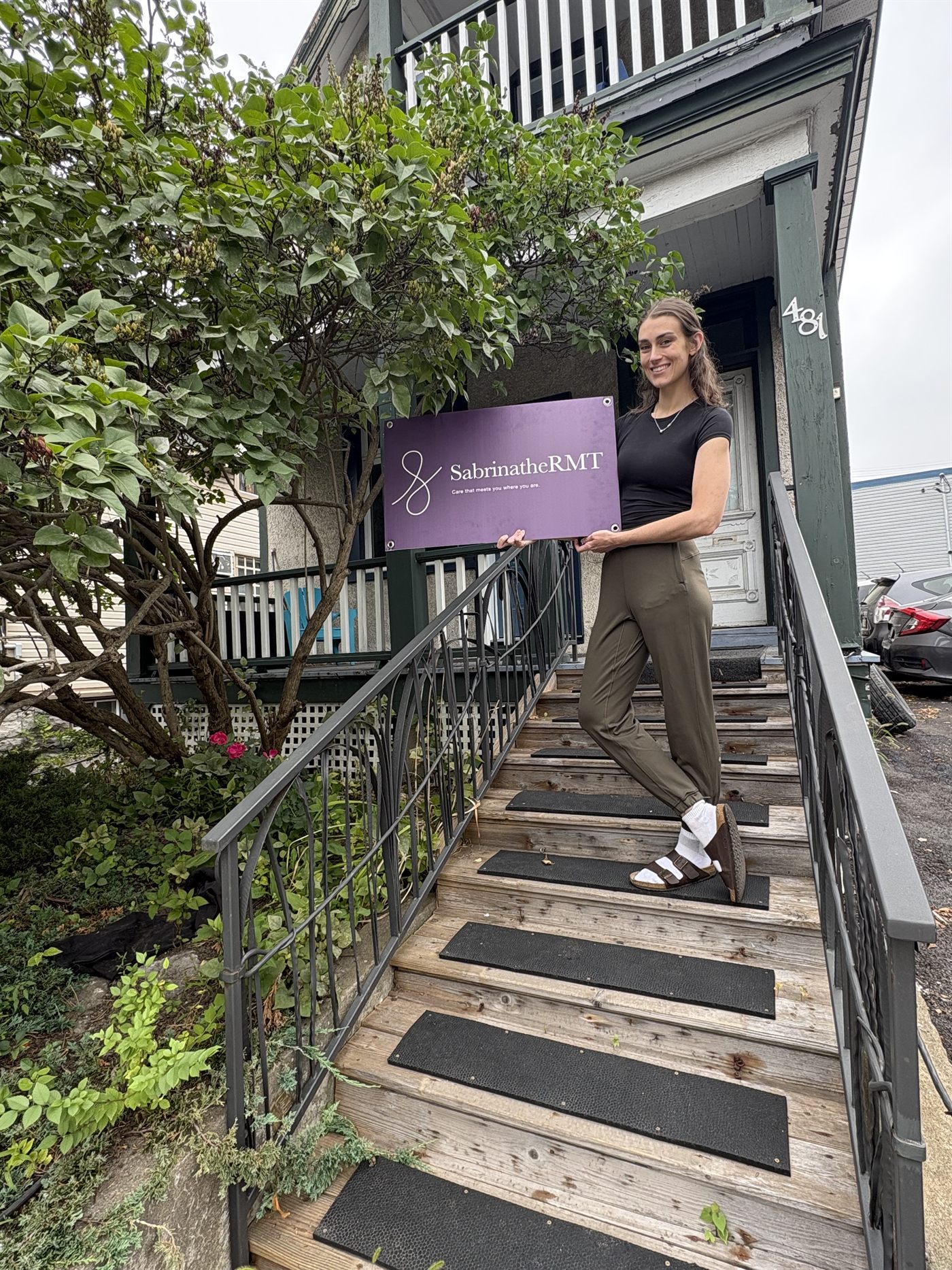 Sabrina standing outside the 481 Gladstone Avenue entrance with a Sabrina The RMT sign.